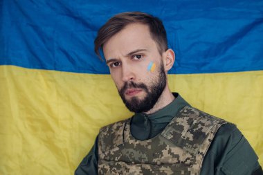 Yüzünde Ukrayna bayrağı olan çelik yelek giymiş öfkeli genç bir adamın portresi. Ukrayna 'da Rus askeri istilası kavramı. Ukrayna ve Avrupa 'da savaş.