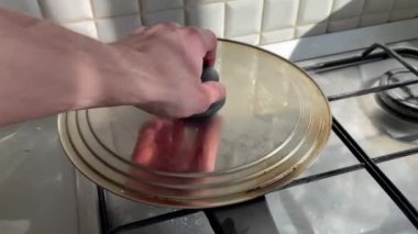Kızartma tavasında tavuk ya da hindi göğsü pişirmek. Adamın eli kızartma tavasının kapağını kaldırır.