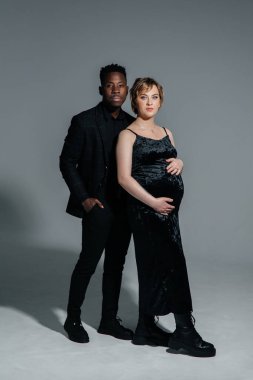 Genç Afrikalı bir adam ve beyaz hamile bir kadın gri arka planda duruyor. Irklar arası evlilik kavramı.