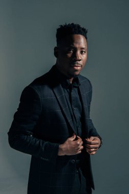 Ceketli genç Afrikalı adam gri arka planda duruyor..