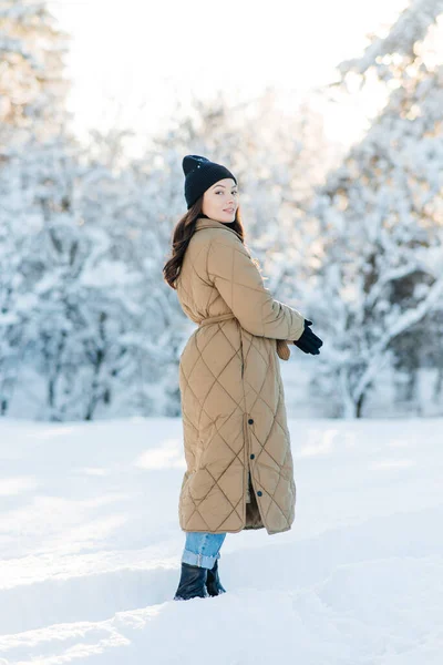 在阳光明媚的冬日里 快乐的年轻微笑的女人走在雪地覆盖的松树丛中 — 图库照片