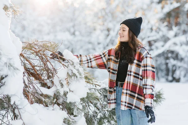 晴れた冬の日に雪に覆われた松の木の間で幸せな若い女性が森を歩く — ストック写真