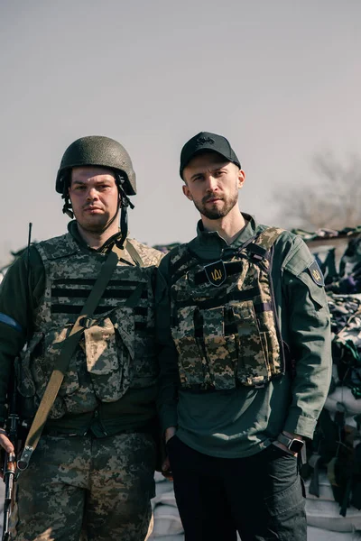 Ukrainian territorial defense warrior stands near volunteer on checkpoint in body armor with automatic gun. Concept of russian military invasion in Ukraine. War in Ukraine and Europe. Closeup.