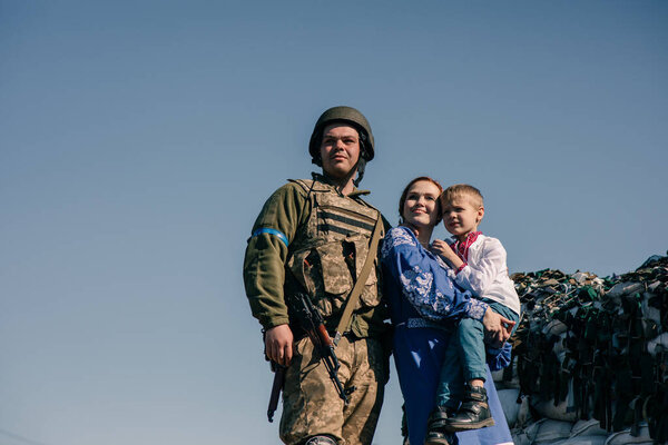 Woman with child boy on her hands stands near Ukrainian soldier on checkpoint against sandbags and sky background. Concept of russian military invasion in Ukraine. War in Ukraine. Children and war.