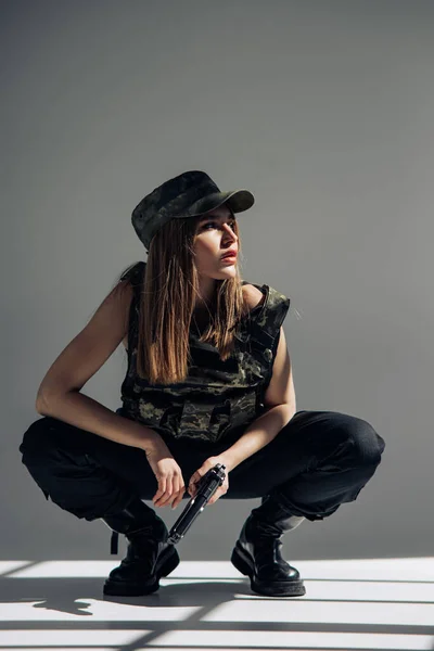 Ung Kvinna Uniform Sitter Och Håller Pistol Handen Mot Grå — Stockfoto