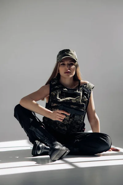 Jonge Vrouw Uniform Zit Houdt Handwapen Haar Hand Tegen Grijze — Stockfoto