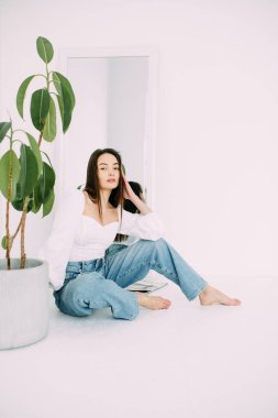 Genç esmer kadın çiçek saksısının yanında oturuyor. Çiçek saksısı aynadaki yansımasının arka planında. Beyaz arkaplan izole görüntü.