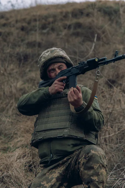 ウクライナ兵はカラシニコフのアサルトライフルから 乾いた草で丘の背景を背景にロシアの敵に狙いを定めている ウクライナにおけるロシアの軍事侵攻の概念 ウクライナとヨーロッパでの戦争 — ストック写真