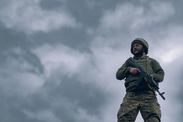 ウクライナ兵は空と雲を背景にカラシニコフのアサルトライフルで立っている ウクライナにおけるロシアの軍事侵攻の概念 ウクライナとヨーロッパでの戦争 コピースペース付き画像 — ストック写真