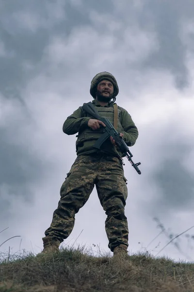 ウクライナ兵は空と雲を背景に手にカラシニコフのアサルトライフルで立っている ウクライナにおけるロシアの軍事侵攻の概念 ウクライナとヨーロッパでの戦争 — ストック写真