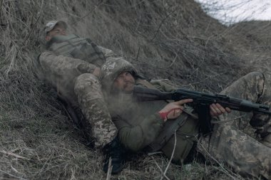 Rus düşmanlarının topçu bombardımanı sırasında iki Ukraynalı asker, Kalaşnikof 'la birlikte kuru çimlere saldırıyor. Ukrayna 'da Rus askeri istilası kavramı. Ukrayna ve Avrupa 'da savaş.