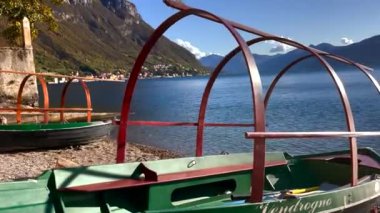 Tekneler Como Gölü kıyısında köyün arka planında, dağlarda ve bulutlu gökyüzünde..