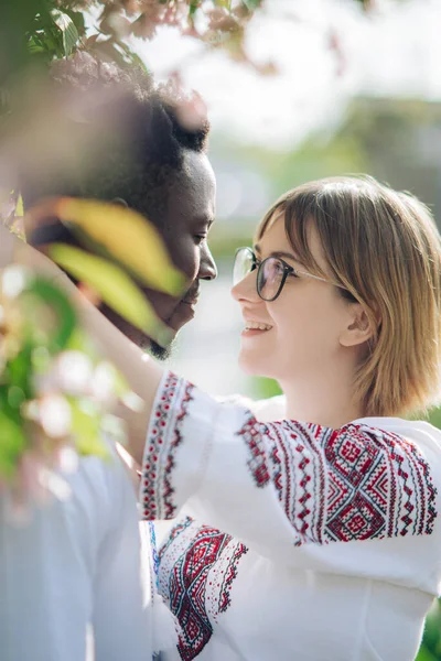 Pareja Interracial Abraza Jardín Primavera Vestida Con Camisas Bordadas Étnicas —  Fotos de Stock