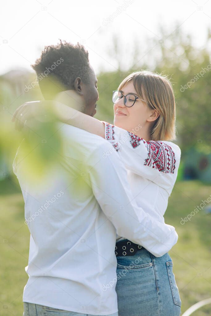 Interracial couple embraces in spring garden dressed in Ukrainian traditional ethnic embroidered shirts. Concept of love relationships and unity between different human races.