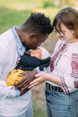 Ukrayna ulusal nakışlı tişörtler giymiş mutlu ırklar arası aile yeni doğan bebeklerini tutuyor ve öpüyor. Irklar arası aile kavramı ve farklı insan ırkları arasındaki birlik.