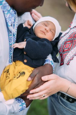 Ukrayna ulusal nakışlı gömlekler giyen mutlu ırklar arası aile yeni doğan bebeklerini kucağında tutuyor. Irklar arası aile kavramı ve farklı insan ırkları arasındaki birlik. Yakın çekim..