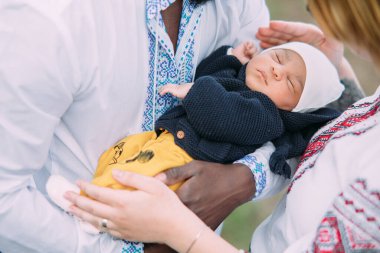 Ukrayna ulusal nakışlı gömlekler giyen mutlu ırklar arası aile yeni doğan bebeklerini kucağında tutuyor. Irklar arası aile kavramı ve farklı insan ırkları arasındaki birlik. Yakın çekim..