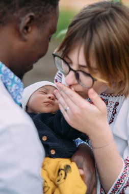 Ukrayna ulusal nakışlı gömlekler giymiş mutlu ırklar arası aile yeni doğmuş bebeklerinin elini tutuyor ve öpüyor. Irklar arası aile kavramı ve farklı insan ırkları arasındaki birlik.