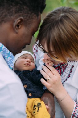 Ukrayna ulusal nakışlı gömlekler giymiş mutlu ırklar arası aile yeni doğmuş bebeklerinin elini tutuyor ve öpüyor. Irklar arası aile kavramı ve farklı insan ırkları arasındaki birlik.