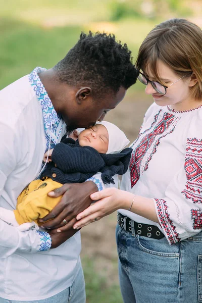 Ukrayna ulusal nakışlı tişörtler giymiş mutlu ırklar arası aile yeni doğan bebeklerini tutuyor ve öpüyor. Irklar arası aile kavramı ve farklı insan ırkları arasındaki birlik.
