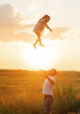 Mutlu çocuklu baba eğleniyor, oynuyor ve gün batımında kızını çayıra atıyor..