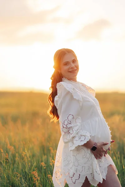 Tânăra Femeie Gravidă Fericită Merge Rochie Albă Printre Pajiști Apusul — Fotografie, imagine de stoc