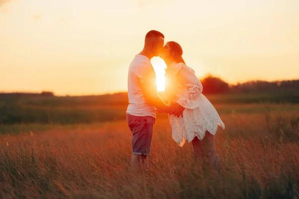 若いです妊娠中の女性と男キス中に外出で牧草地に日没 — ストック写真
