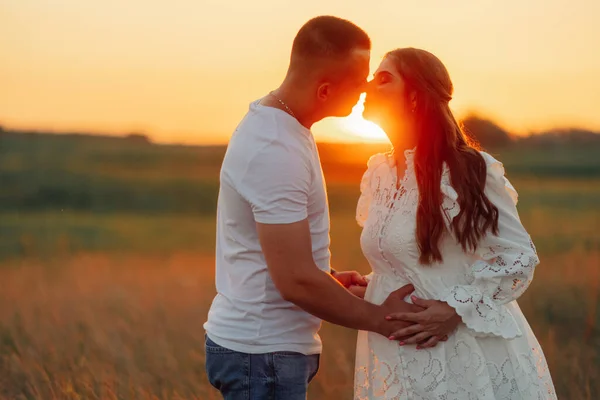 日没時に牧草地で外出中の若い妊婦と男のキス — ストック写真