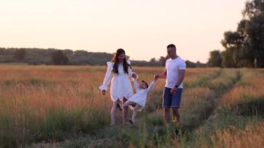 Çocuklu mutlu ebeveynler eğleniyor, oynuyorlar ve kızlarının elini kaldırıyorlar..