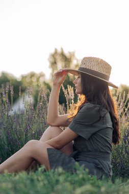 Şapkalı genç kadın oturur ve lavanta tarlasında dinlenir. Çiçek açarak eğlenir..
