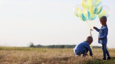 Mutlu iki ikiz kardeş hava balonlarıyla çayırda oynuyorlar. Ukrayna ulusal nakışlı gömlekler giyiyorlar. Kopyalama alanı olan video.
