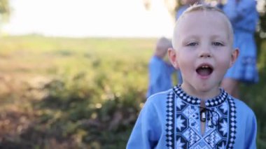 Mutlu küçük çocuk çayırda ailesinin geçmişine karşı yürüyor. O, Ukrayna ulusal nakışlı gömlek giymiştir..