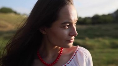 Portrait of young Ukrainian woman looking at side in traditional national embroidered shirt and necklace on meadow. Ethnic ukrainian national clothes style.
