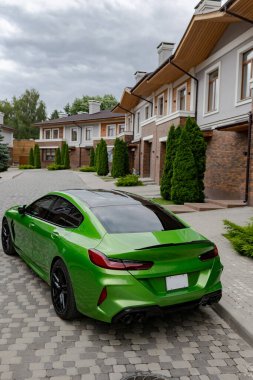 Modern green car is on parking near beautiful house with landscaping. Back and top view.
