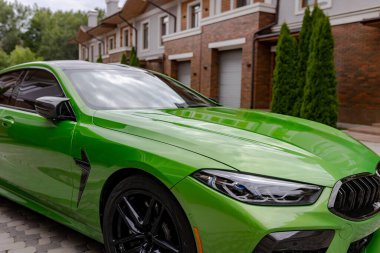 Modern green car is on parking near garage gate of beautiful house.