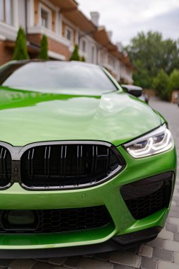 Closeup view to headlights and radiator grill of modern green car standing near house.