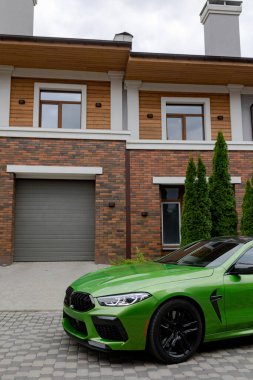 Modern green car is on parking near garage gate of beautiful house.