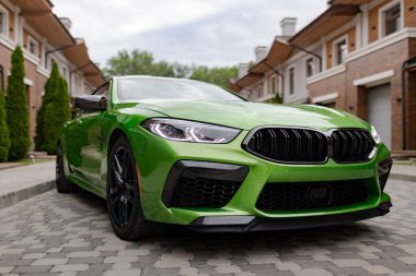 Modern green car is on parking near beautiful house with landscaping.