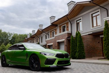 Modern green car is on parking near garage gate of beautiful house.