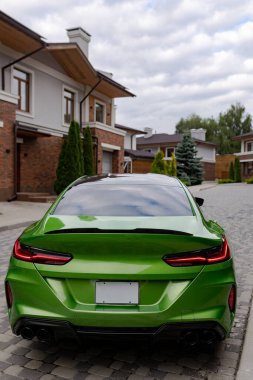 Modern green car is on parking near beautiful house with landscaping. Back view.
