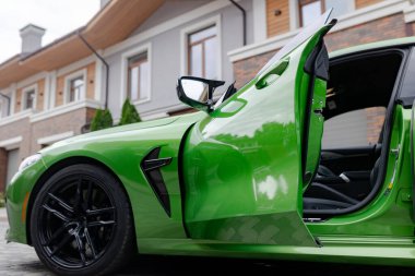 Modern green car with opened door is on parking near garage of house.