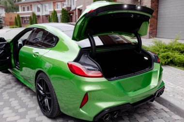 Modern green car with opened trunk and door is on parking near garage gate of house.