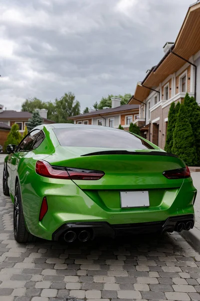 Modern green car is on parking near beautiful house with landscaping. Back view.