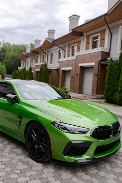Modern green car is on parking near garage gate of beautiful house.
