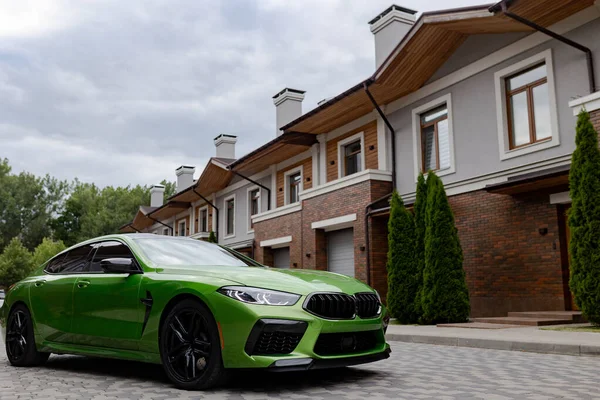 Modern green car is on parking near garage gate of beautiful house.