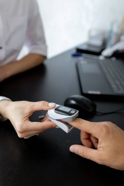 Woman doctor measures by pulse oximeter blood oxygen saturation for patient in clinic. Test, diagnostic, healthcare, medical service. Coronavirus covid-19 pandemic.