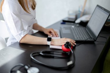 Woman doctor sits at desk and works at laptop in clinic against background of medical equipment. Test, professional consult, disease diagnostic, healthcare, medical service.