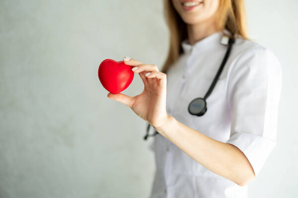 Женщина-кардиолог держит и показывает красную модель сердца в клинике. Концепция диагностики и лечения сердечно-сосудистых заболеваний. Здравоохранение, медицинское обслуживание.