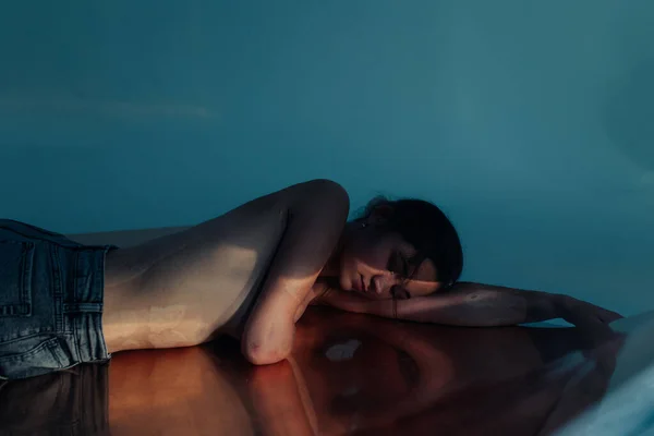 Beautiful young woman with amputee arm and scars from burn on her body poses lying topless. There is visible her reflection on surface. The concept of a fulfilling life of persons with disabilities.