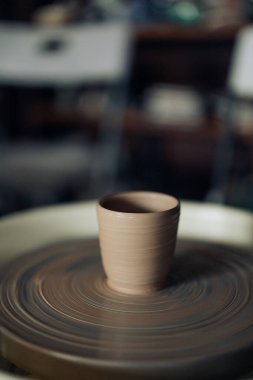 Handmade earthenware cup on pottery wheel in workshop closeup.